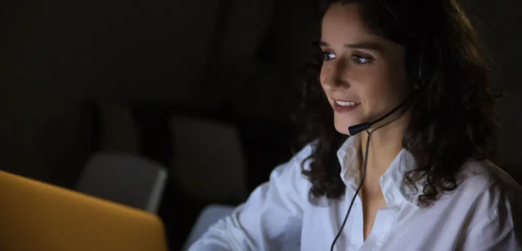 Atendente sorridente com headset trabalhando no computador à noite, ilustrando na prática como funciona URA reversa em centrais de atendimento modernas