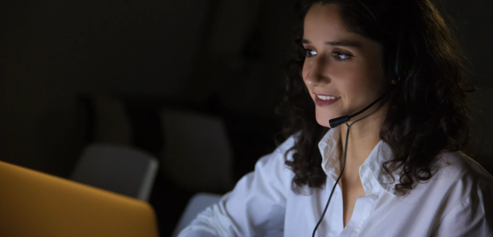 Atendente sorridente com headset trabalhando no computador à noite, ilustrando na prática como funciona URA reversa em centrais de atendimento modernas