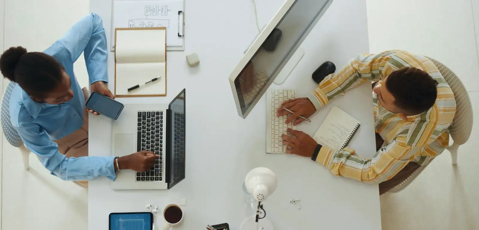 Dois profissionais usando computador e celular para organizar atendimentos via WhatsApp corporativo em um ambiente de trabalho moderno