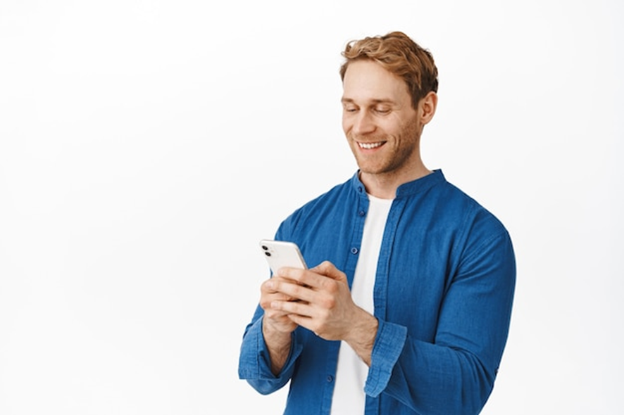 Homem sorridente olhando para o smartphone, possivelmente lendo ou digitando um SMS.