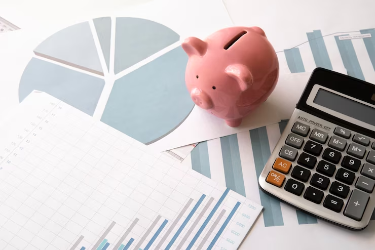 Gráficos financeiros acompanhados de um cofrinho rosa e uma calculadora, simbolizando a análise e planejamento financeiro.