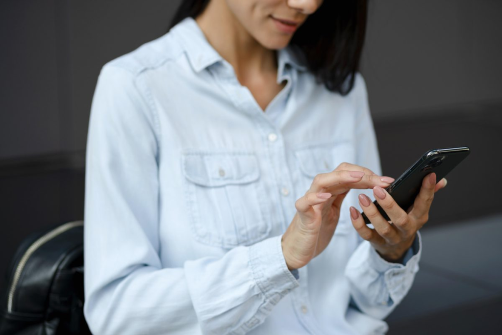 Uma mulher casualmente vestida digitando em seu smartphone, talvez enviando uma mensagem ou navegando na web, em um cenário urbano moderno.