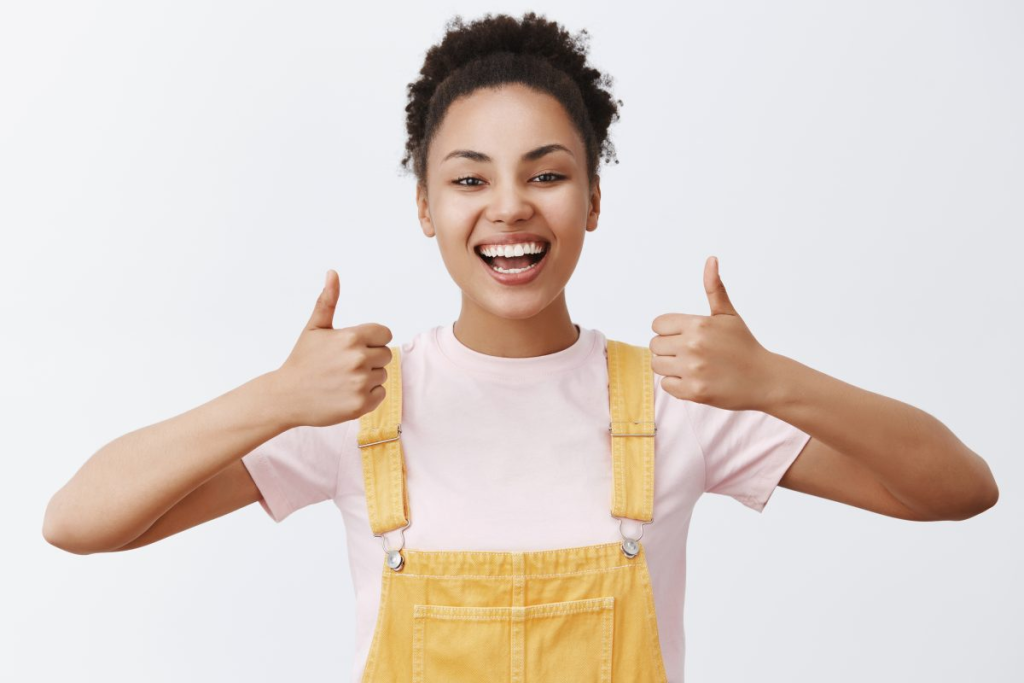 Uma mulher jovial em roupas casuais fazendo sinal de positivo com as duas mãos, transmitindo uma mensagem de satisfação, aprovação e atitude positiva.