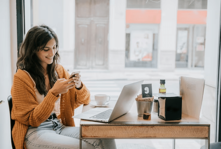 Mulher sorridente verifica mensagens do WhatsApp enquanto toma café em uma cafeteria, ilustrando a comunicação casual e a conexão constante.
