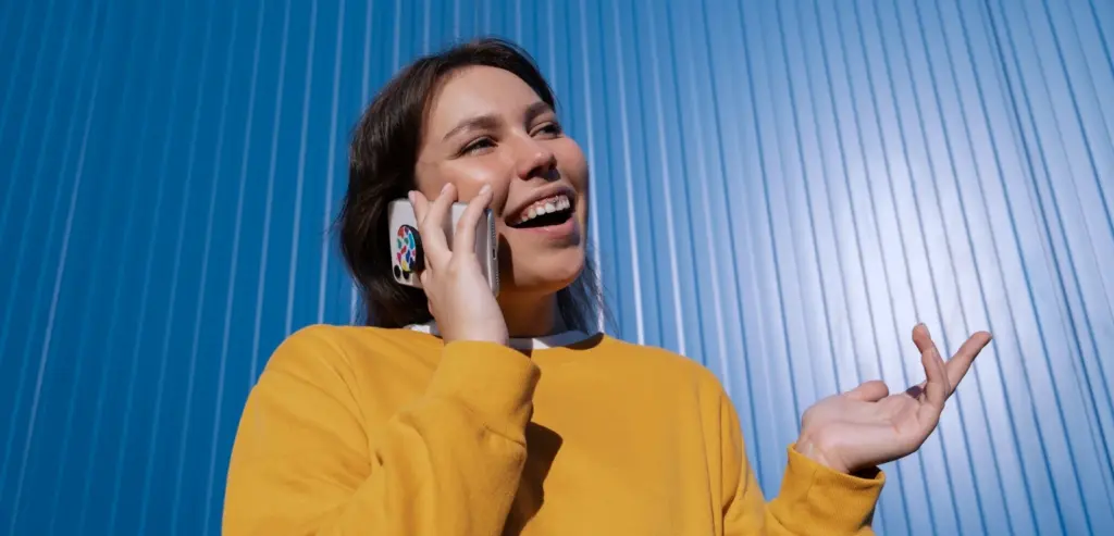 Mulher sorridente falando ao telefone em frente a uma parede azul, representando comunicação moderna e eficiente com tecnologia 0800 VoIP.
