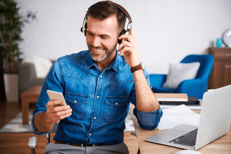 Homem sorridente com fone de ouvido usando um cartão de crédito e laptop, possivelmente gerenciando finanças ou realizando uma transação online.


