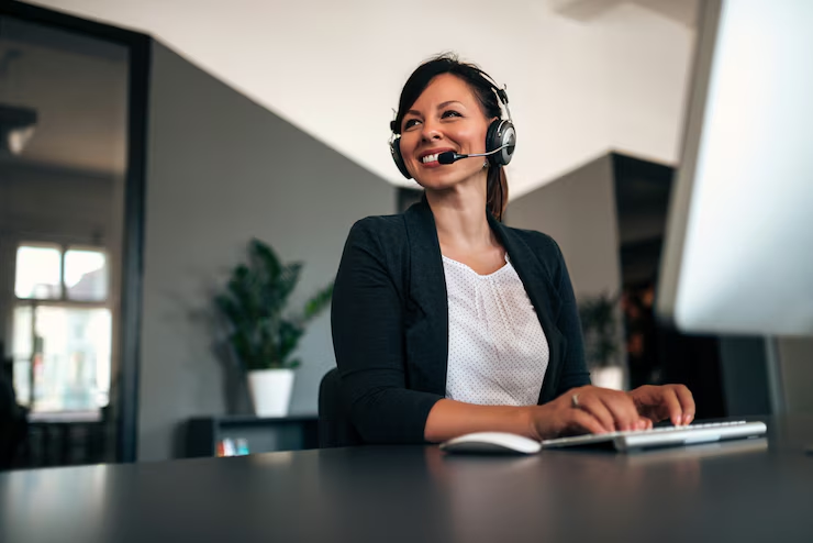 Operadora de call center sorrindo enquanto trabalha em seu computador, transmitindo a postura amigável e atenciosa típica desse setor.
