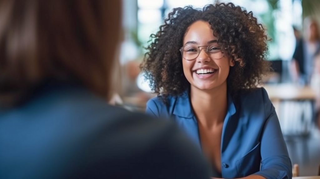 Mulher com cabelos encaracolados e óculos sorrindo durante uma reunião, potencialmente discutindo sobre o uso de software colaborativo ou CRM.