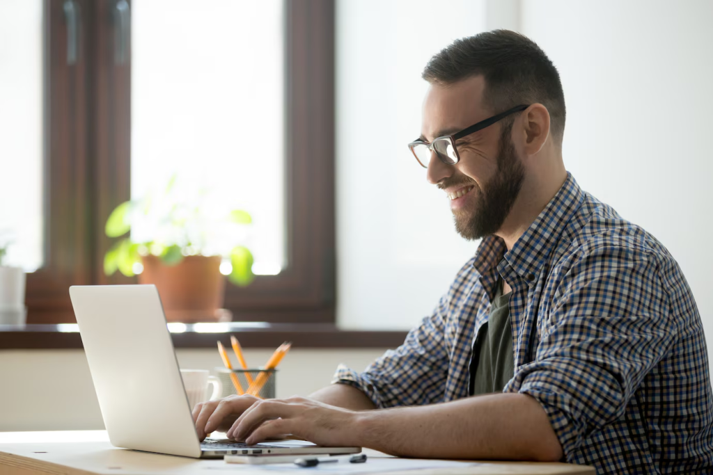um homem é mostrado focado em seu trabalho em um laptop, representando um profissional gerenciando atendimento ao cliente ou outras tarefas em um ambiente digital.