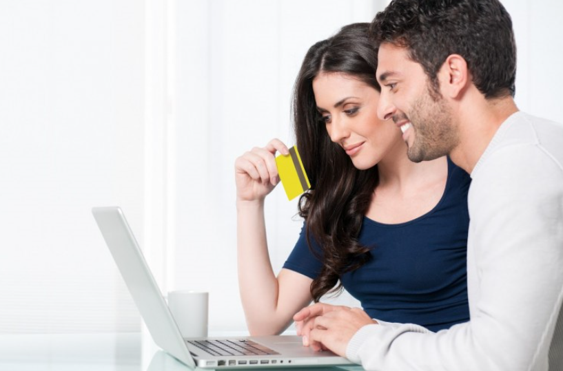 Um casal olhando para um laptop e segurando um cartão de crédito, possivelmente realizando uma compra online.