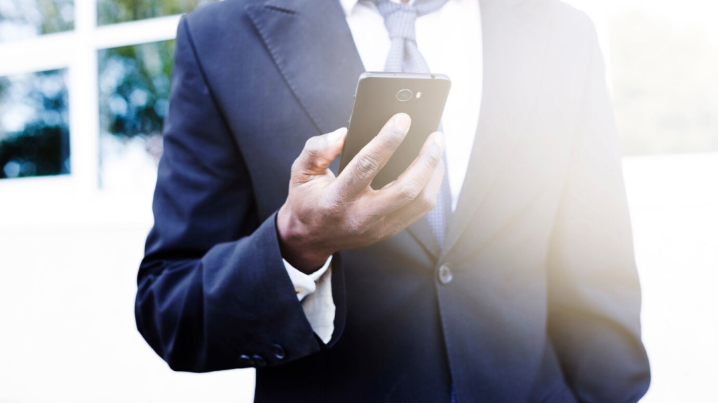 Homem de negócios verificando seu smartphone enquanto caminha ao ar livre, focando na conectividade e na mobilidade corporativa.