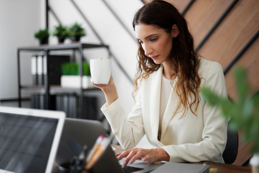 Mulher empresária concentrada trabalhando em seu laptop em um escritório moderno enquanto toma um café.