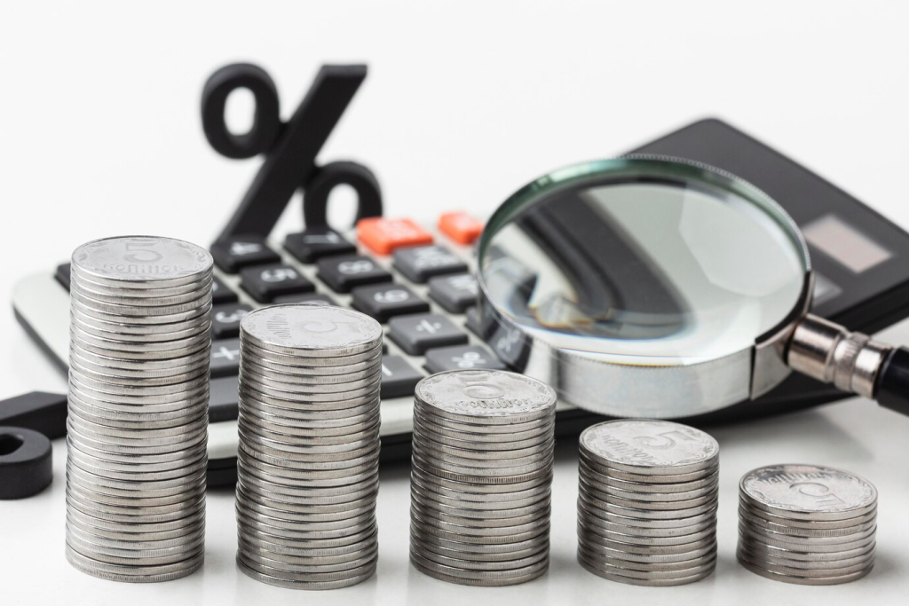 Empilhamento progressivo de moedas ao lado de uma lupa e uma calculadora, simbolizando o crescimento econômico e a gestão financeira inteligente.