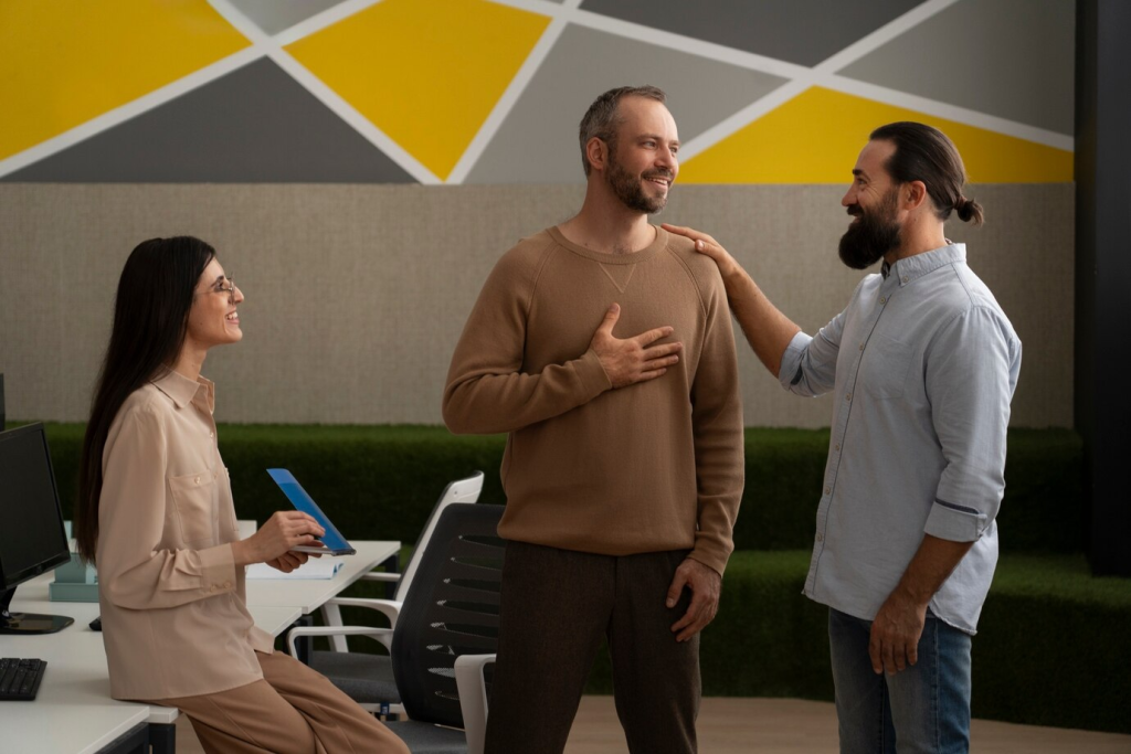 Imagem de três colegas de trabalho em um ambiente de escritório descontraído, com um aperto de mãos, destacando a importância da comunicação pessoal e da parceria no mundo dos negócios, que pode ser fortalecida com o uso de tecnologia de comunicação avançada como o DID.
