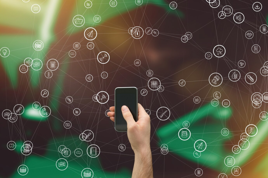 Rede de ícones de comunicação digital sobreposta a uma imagem borrada de uma pessoa segurando um smartphone, simbolizando conexão global.