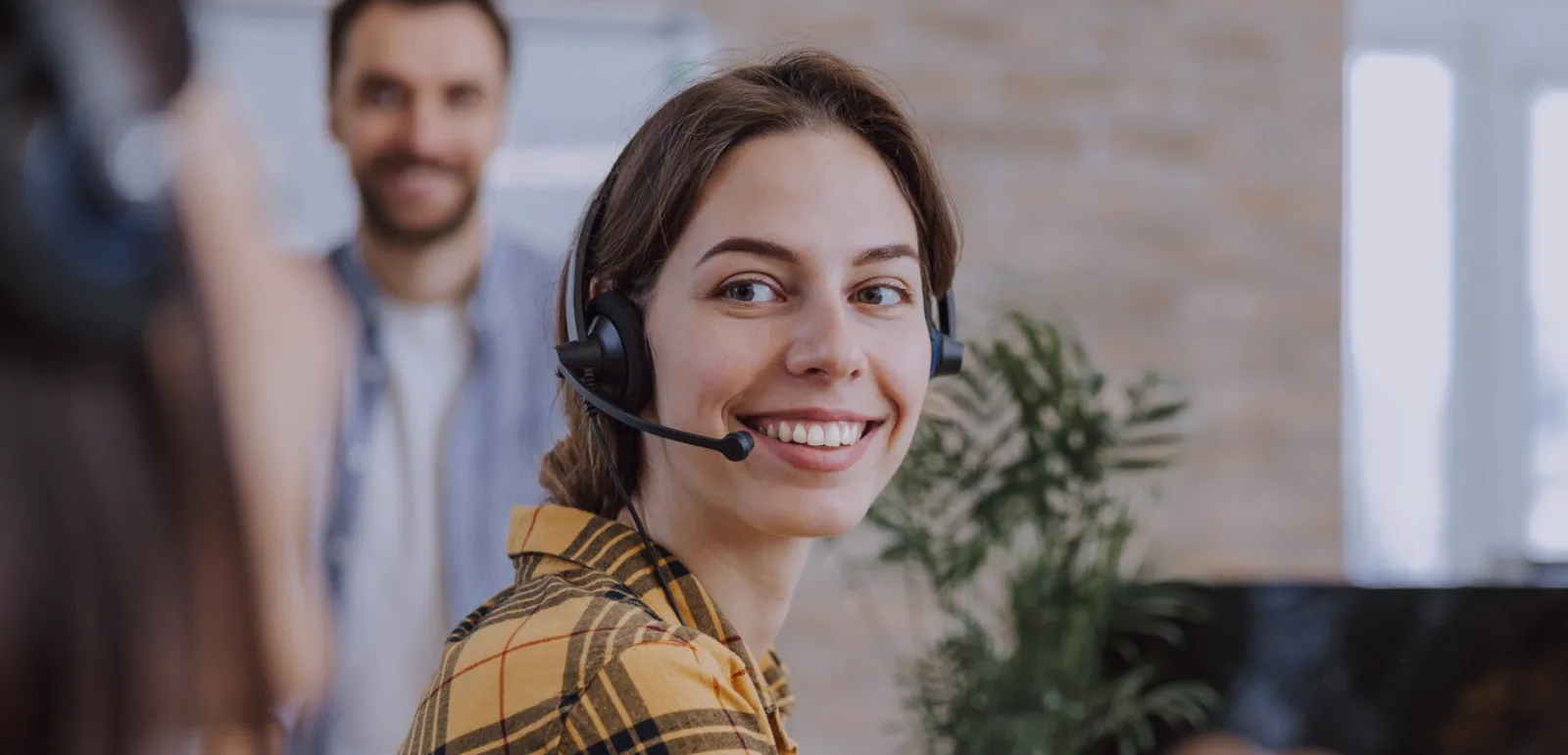 Mulher usando headset e sorrindo enquanto realiza atendimento ao cliente em ambiente moderno