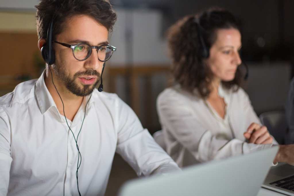 Operador de call center masculino usando fones de ouvido e óculos, trabalhando em um ambiente de escritório, destacando a terceirização de atendimento ao cliente.