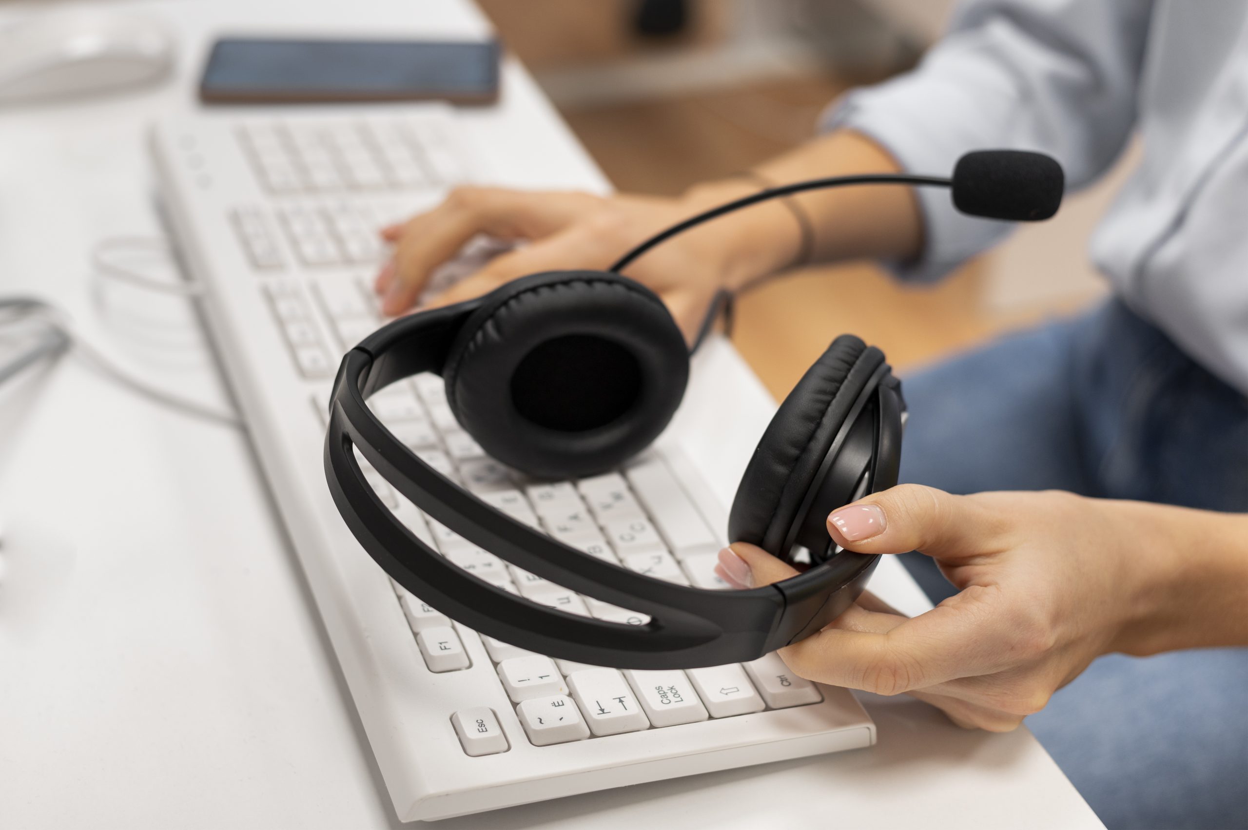 Imagem de uma pessoa trabalhando em um call center, digitando em um teclado branco enquanto segura um par de fones de ouvido com microfone.