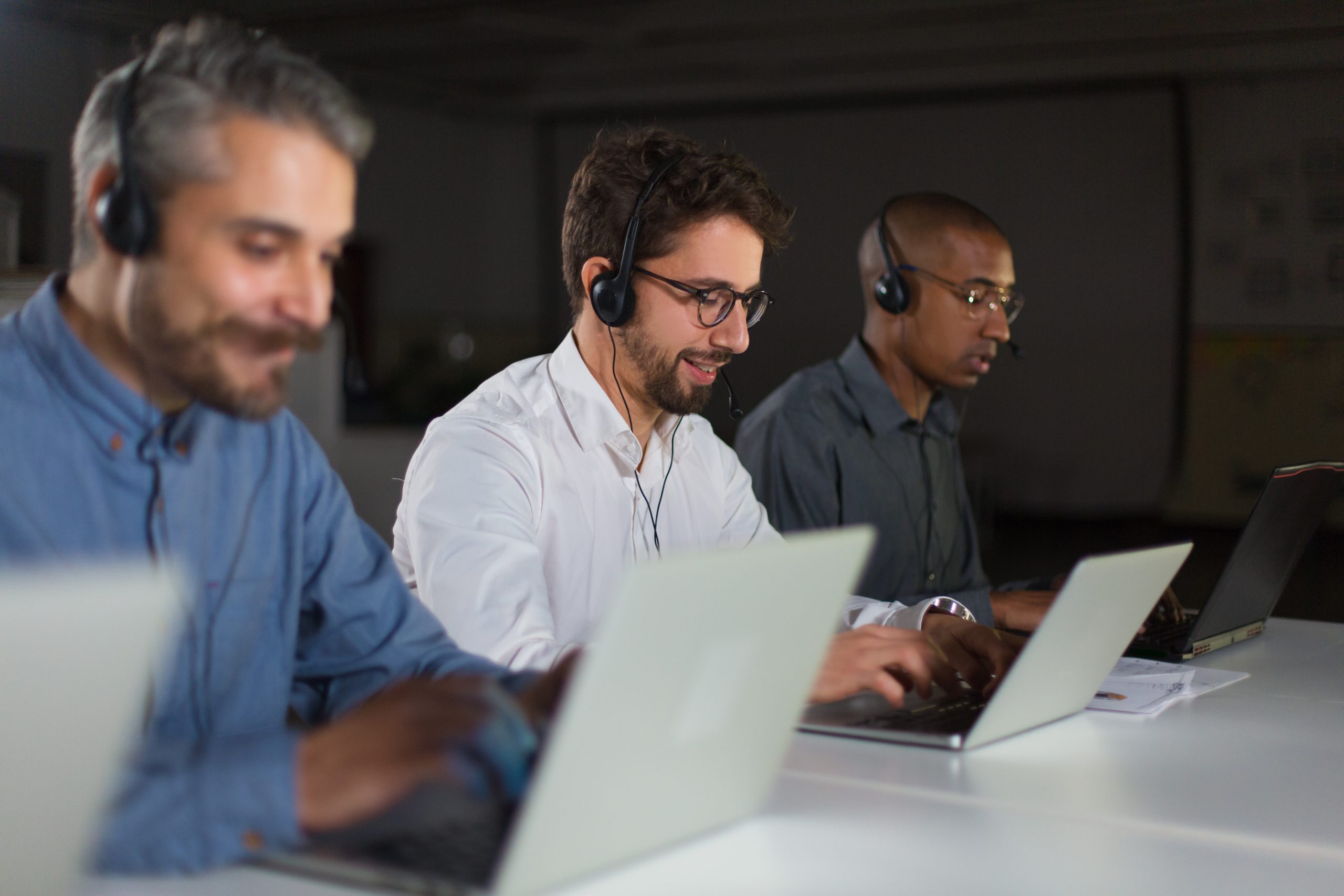 Equipe de operadores de call center trabalhando em laptops, todos usando headsets. Eles estão concentrados e engajados, demonstrando um ambiente de trabalho colaborativo e eficiente.