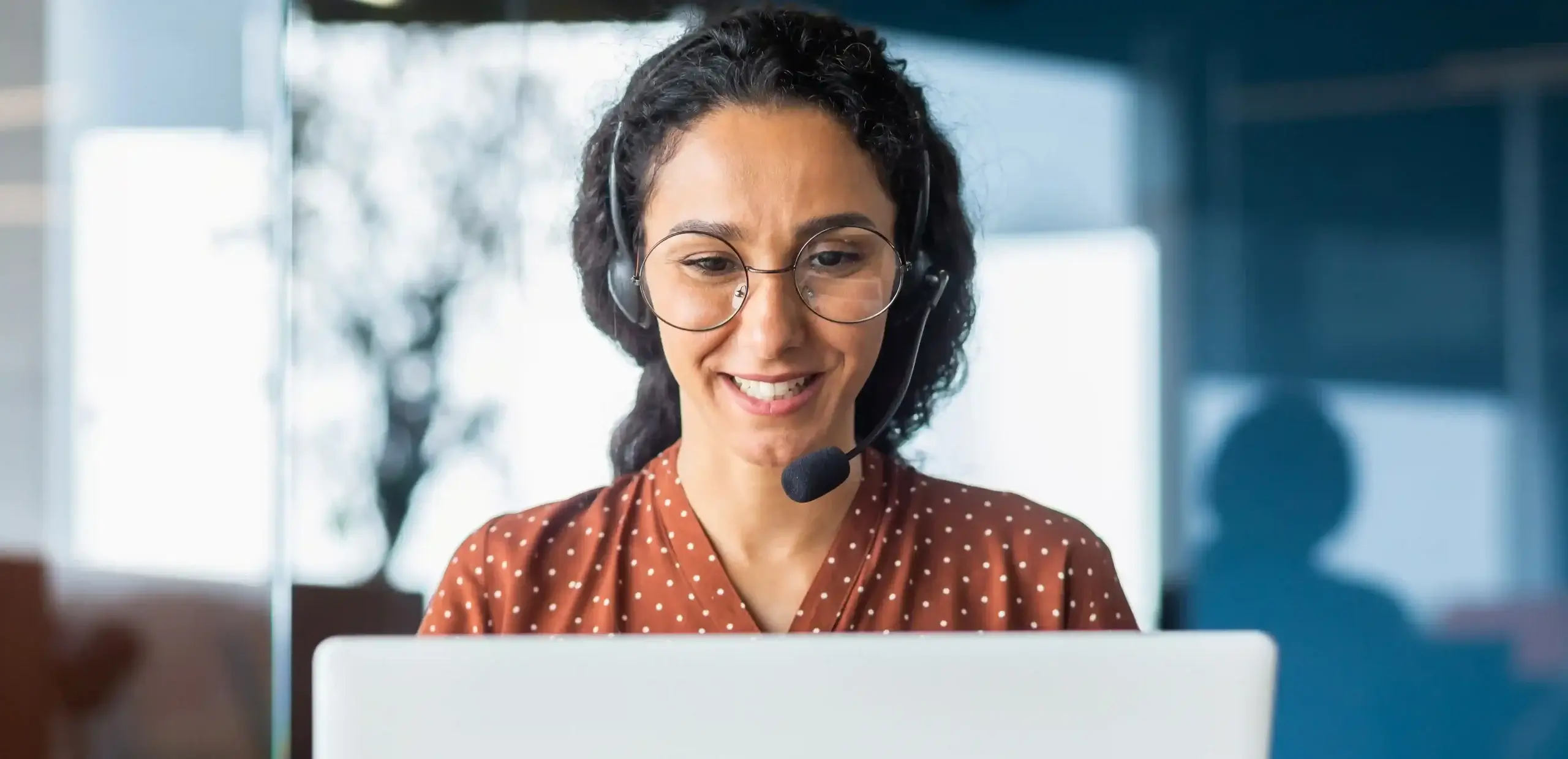 Mulher sorridente com headset atendendo clientes pelo computador, representando a flexibilidade e eficiência do PABX em nuvem para equipes de atendimento.