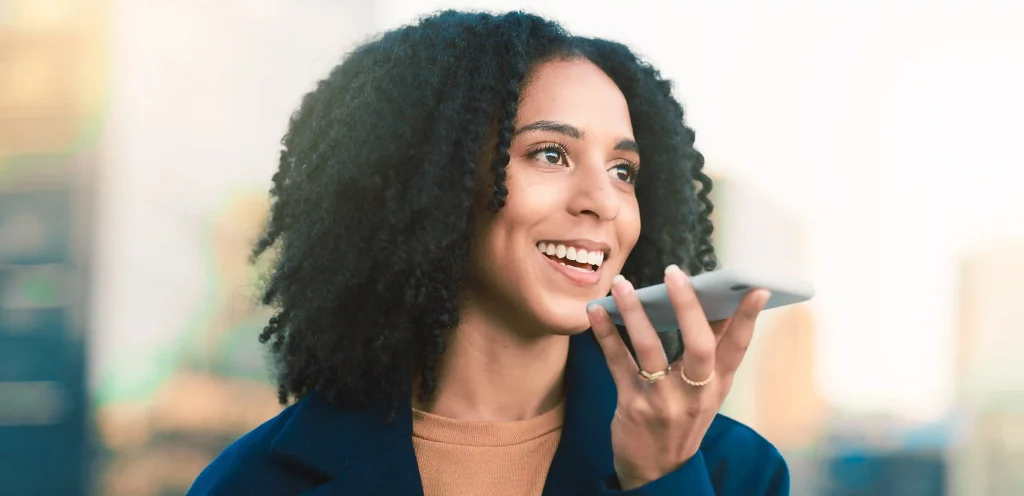 Mulher sorridente falando ao celular por comando de voz, representando o uso do recurso Click to Call para facilitar o contato direto com empresas.