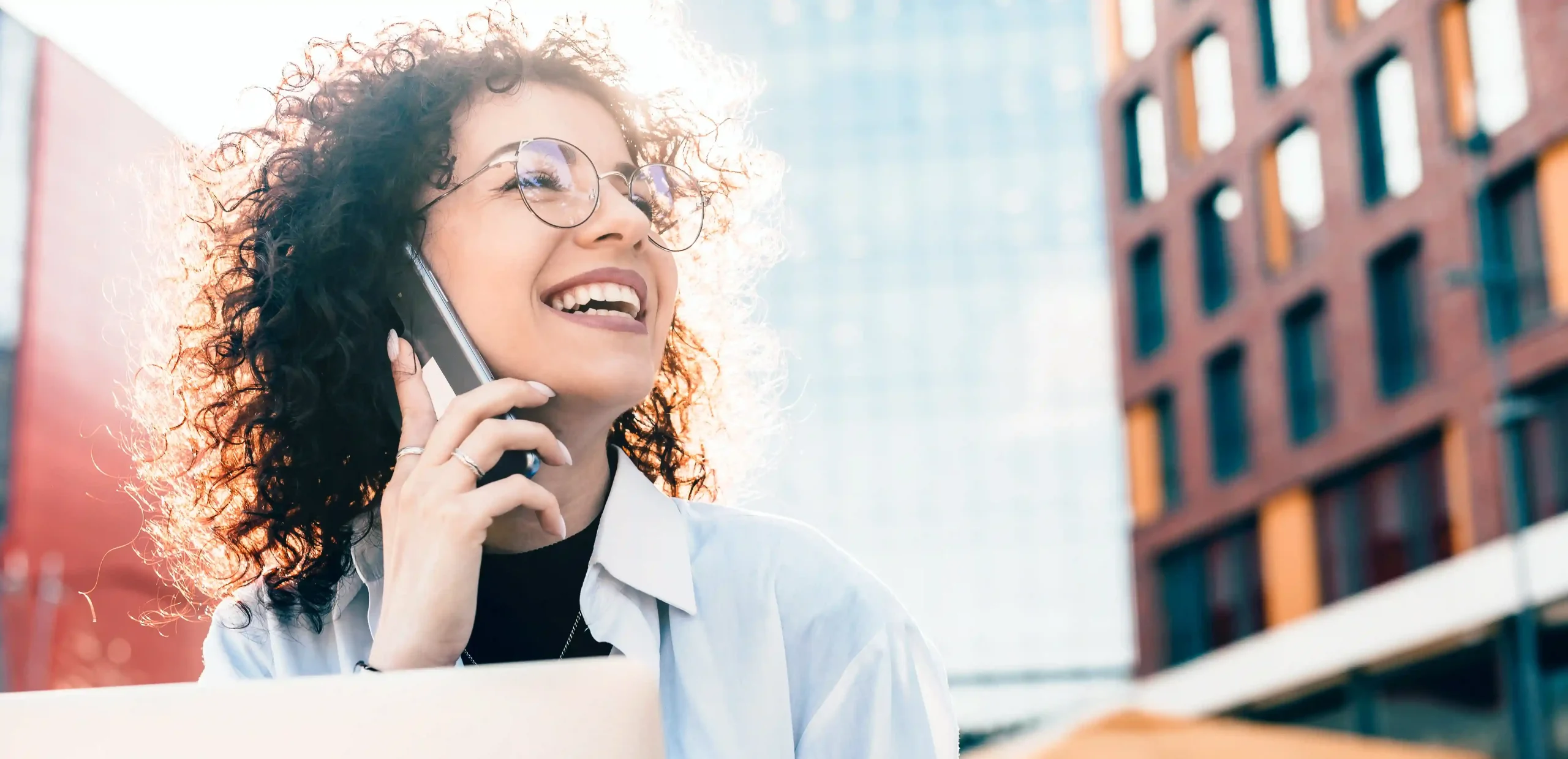Mulher sorridente falando ao celular ao ar livre, representando o impacto das conversões em um clique com a funcionalidade de Click to Call na comunicação moderna.