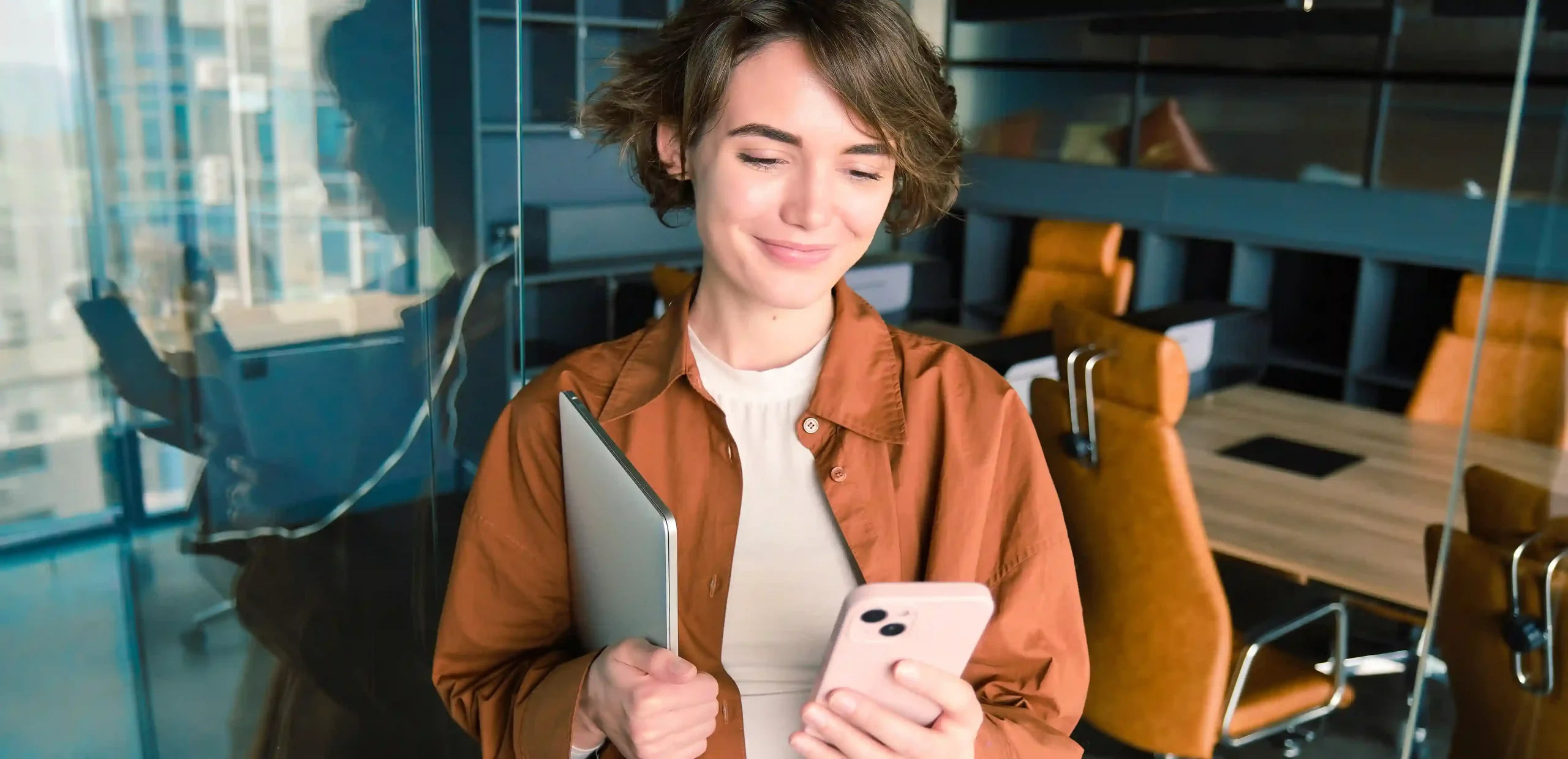 Mulher sorrindo enquanto usa o celular em um ambiente corporativo, representando o uso da API oficial WhatsApp para comunicação empresarial eficiente.