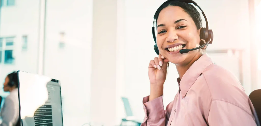 Mulher sorridente com headset trabalhando em atendimento ao cliente em um escritório, representando boas práticas de pós-atendimento para oferecer uma experiência de qualidade.
