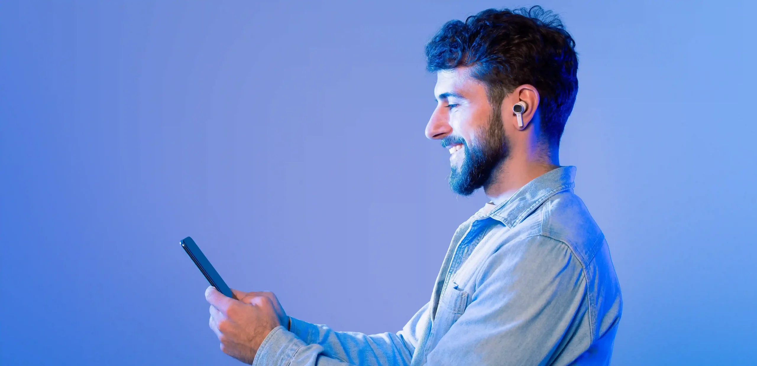 Homem sorridente com fone de ouvido interagindo com smartphone em fundo azul, representando como um chatbot pode impulsionar suas vendas ao oferecer atendimento ágil e eficaz.