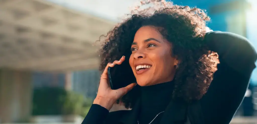 Mulher sorridente falando ao telefone, representando os benefícios da URA (Unidade de Resposta Audível) no atendimento automatizado das empresas.