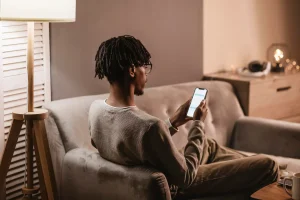 Homem sentado em casa usando o celular para entrar em contato com o SAC, representando um atendimento ao cliente acessível e digital