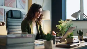 Mulher sorridente em chamada de vídeo no notebook, em ambiente corporativo, simbolizando colaboração e planejamento em estratégias de omnichannel marketing