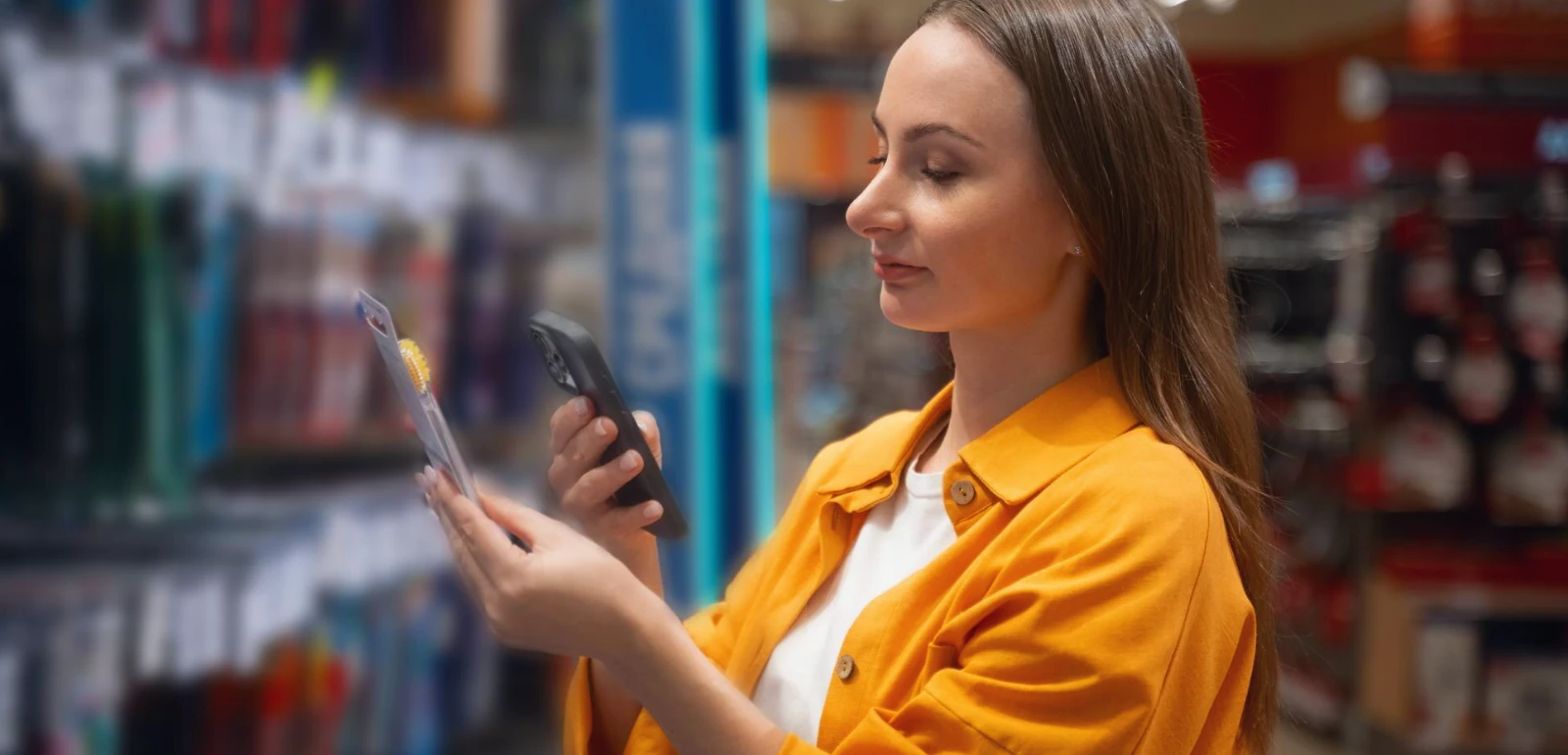 Mulher em loja física usando o celular para comparar produto, representando a experiência integrada do atendimento omnichannel no varejo