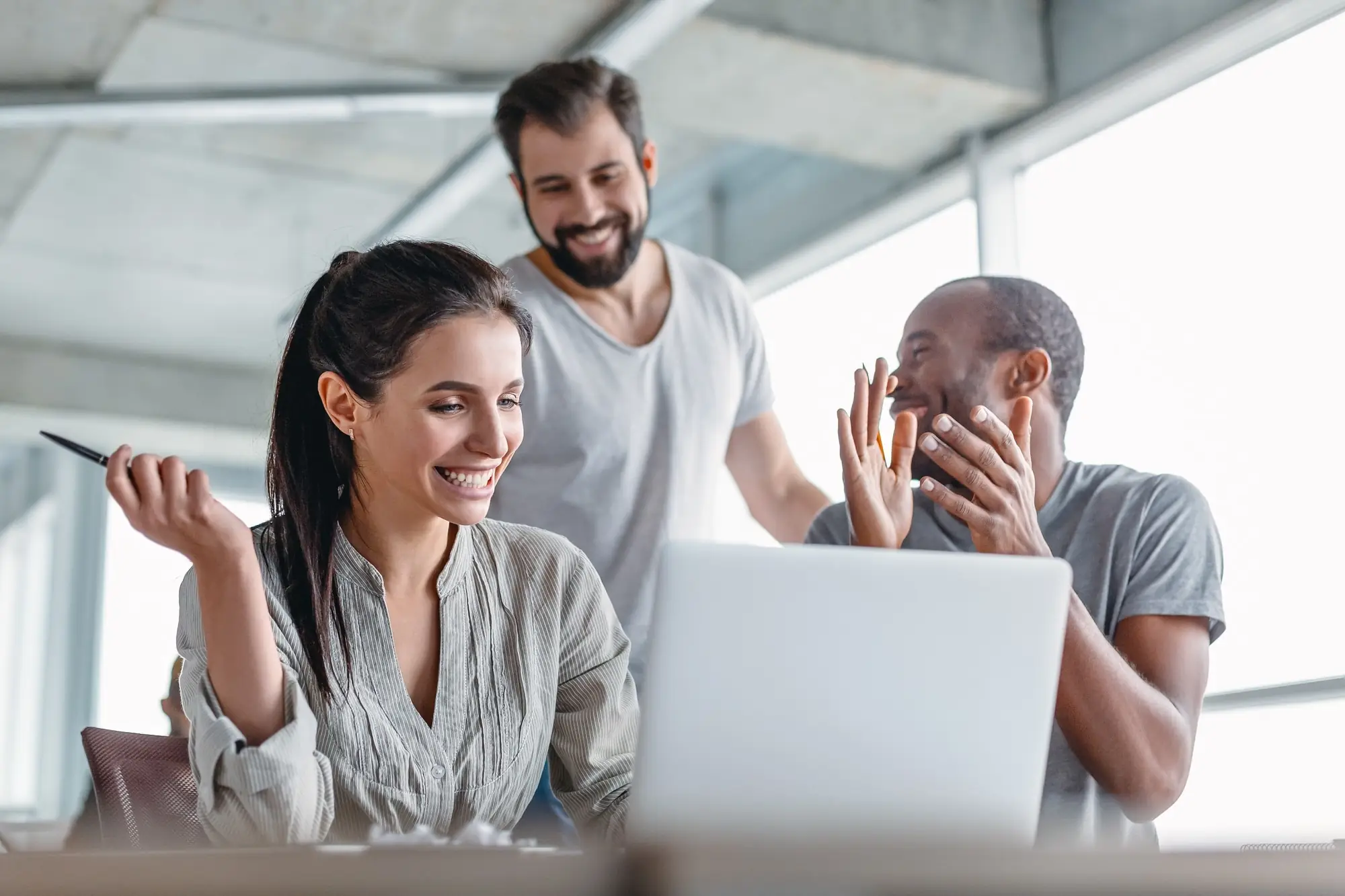 rês profissionais felizes em frente ao notebook em ambiente moderno, celebrando os resultados de uma estratégia omnichannel aplicada com sucesso
