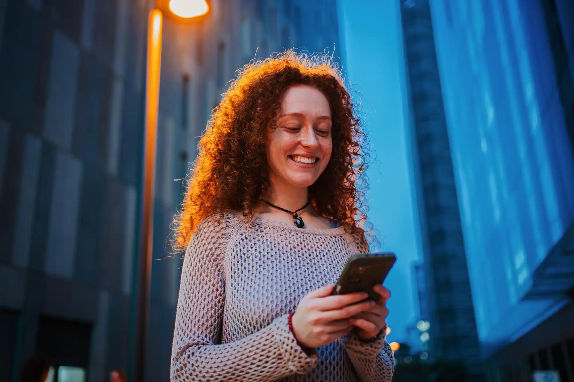 Mulher sorridente enviando mensagem em massa no WhatsApp à noite na cidade