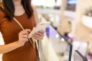 Mulher usando smartphone em shopping, representando o uso de canais digitais integrados ao ambiente físico no atendimento omnichannel