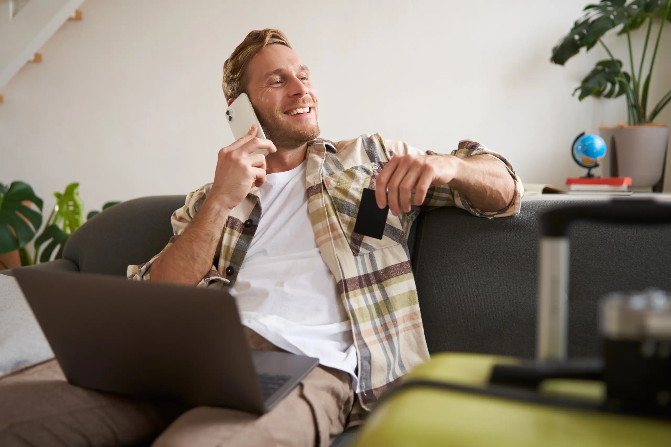 Agentes de IA para gerar mais vendas em 2026 ilustrados por homem sorrindo ao telefone, usando notebook e segurando cartão de crédito em casa