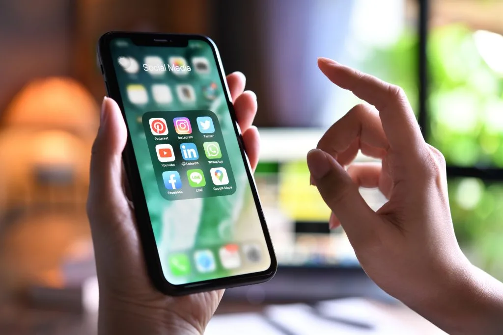 uma pessoa segura um smartphone, exibindo aplicativos de mídia social com destaque, com o WhatsApp em primeiro plano. Destaca o papel central dos aplicativos de mensagens na comunicação moderna.